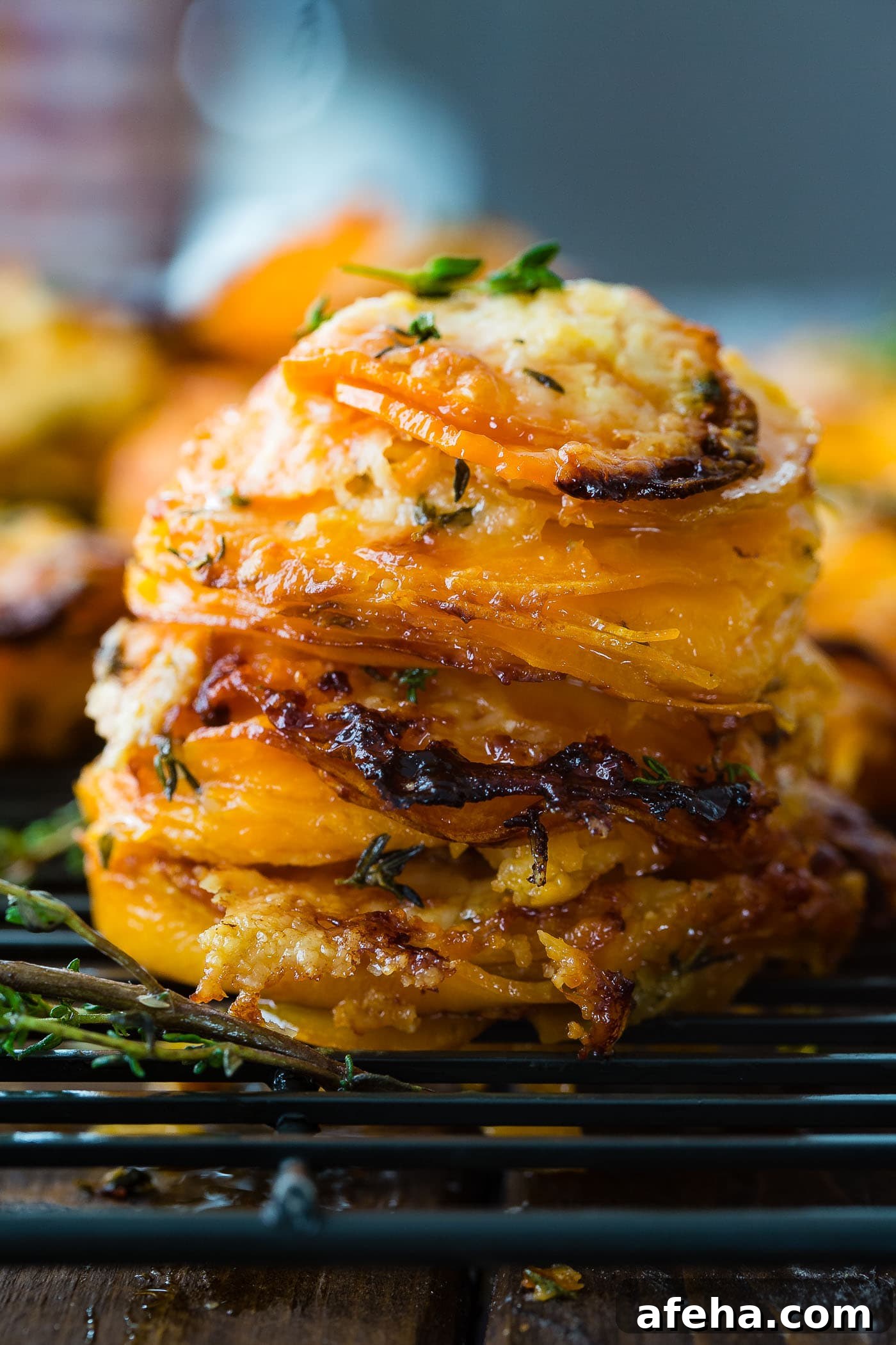 A photo of a stack of thinly sliced sweet potatoes layered with gruyere and parmesan cheese and topped with fresh thyme.