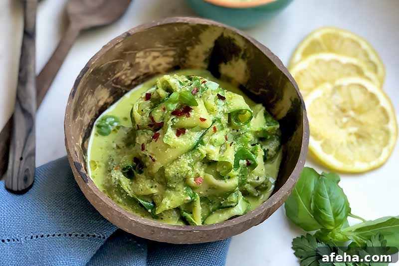 Horizontal image of a wooden bowl filled with a pile of cooked thinly sliced vegetables covered in a vibrant green sauce and fresh herb garnish next to a blue towel, wooden spoons, lemon slices.