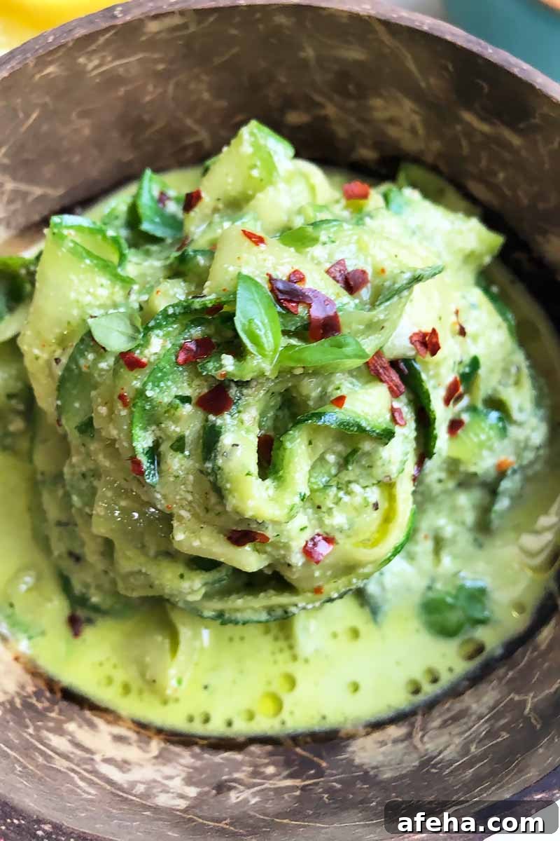 Vertical close-up image of a wooden bowl filled with thinly sliced vegetable noodles mixed in a pesto alfredo.