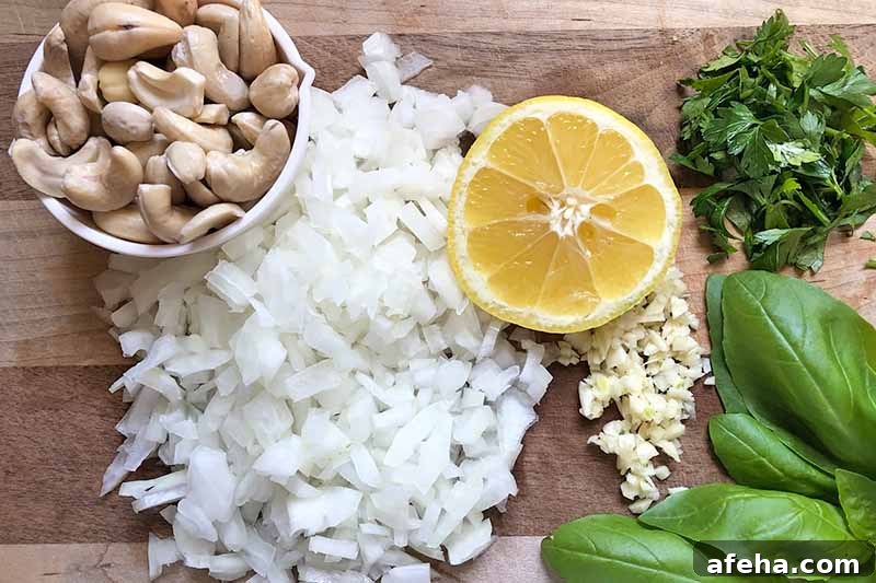Horizontal image of chopped onions, a bowl of cashews, a wedge of lemon, mined garlic, and herbs.