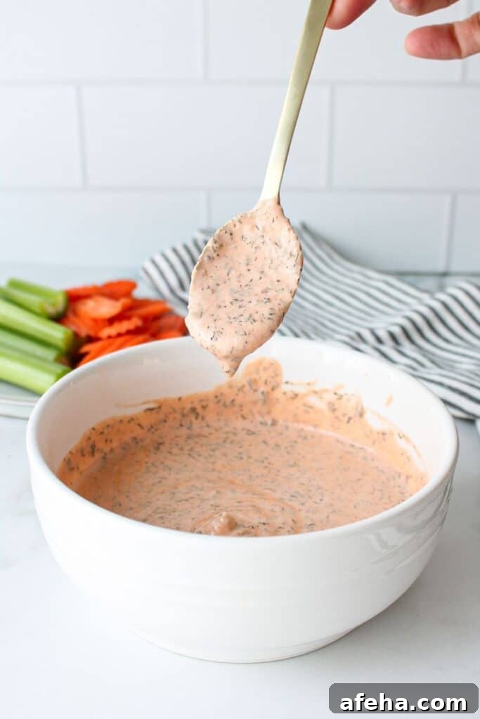 A spoonful of buffalo ranch sauce being held above a bowl full of sauce.
