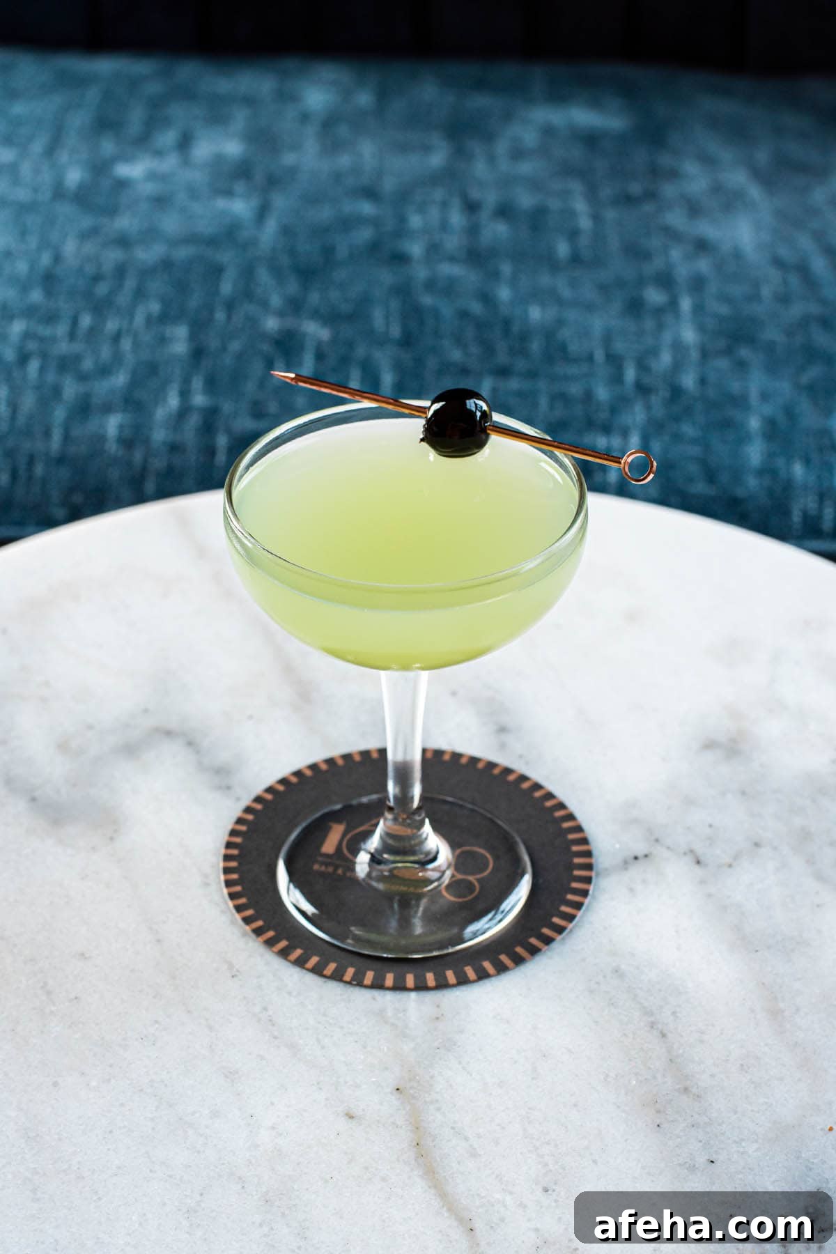 A classic Last Word cocktail sitting on a marble table, garnished with a branded cherry.