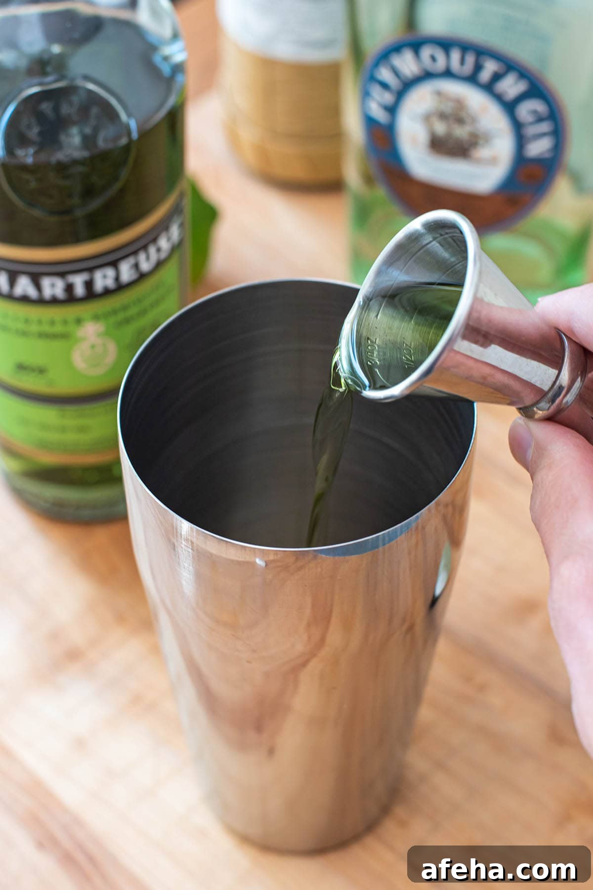 Pouring Green Chartreuse liqueur into a cocktail shaker with a double jigger.