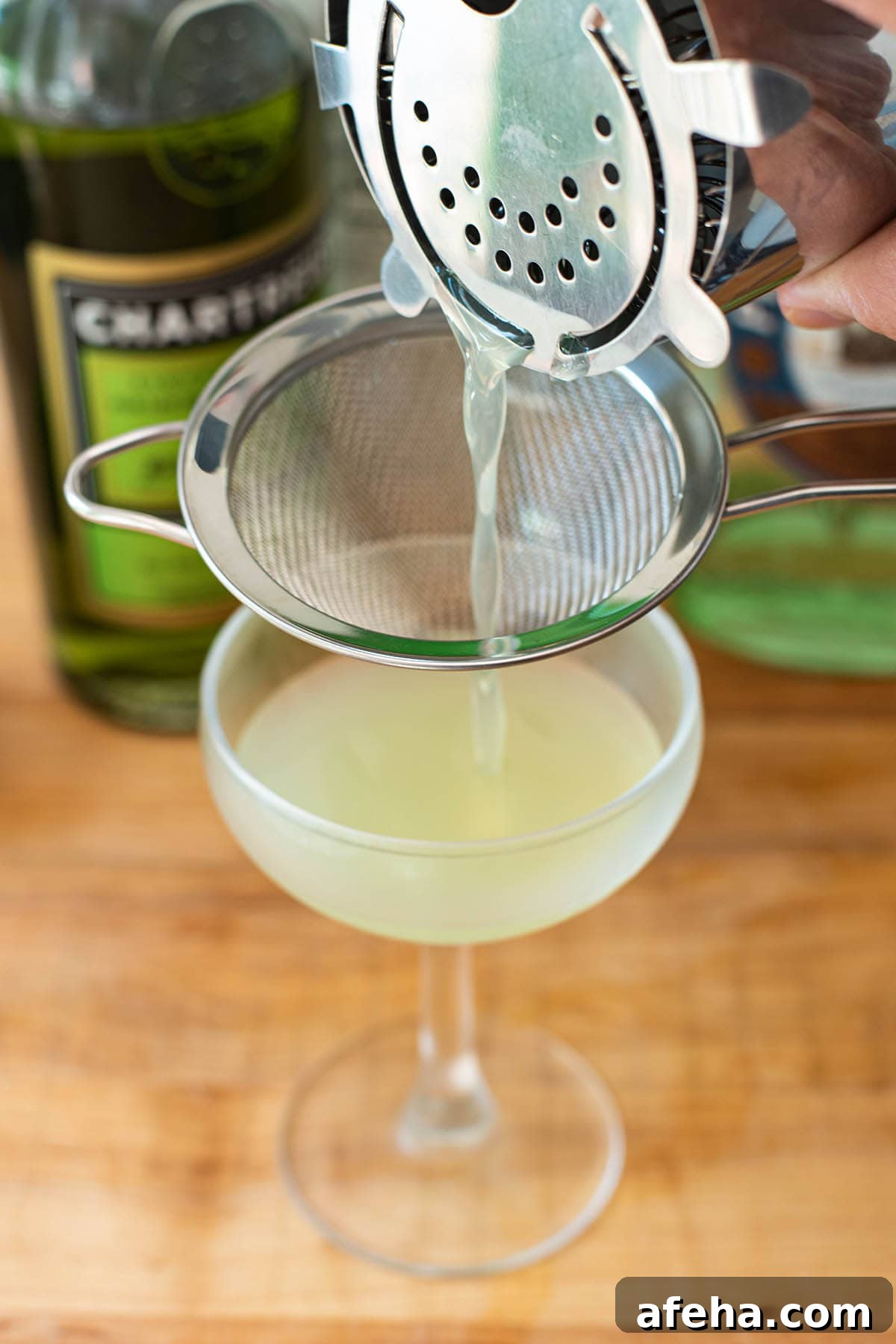 Double straining a Last Word cocktail into a chilled coupe glass.