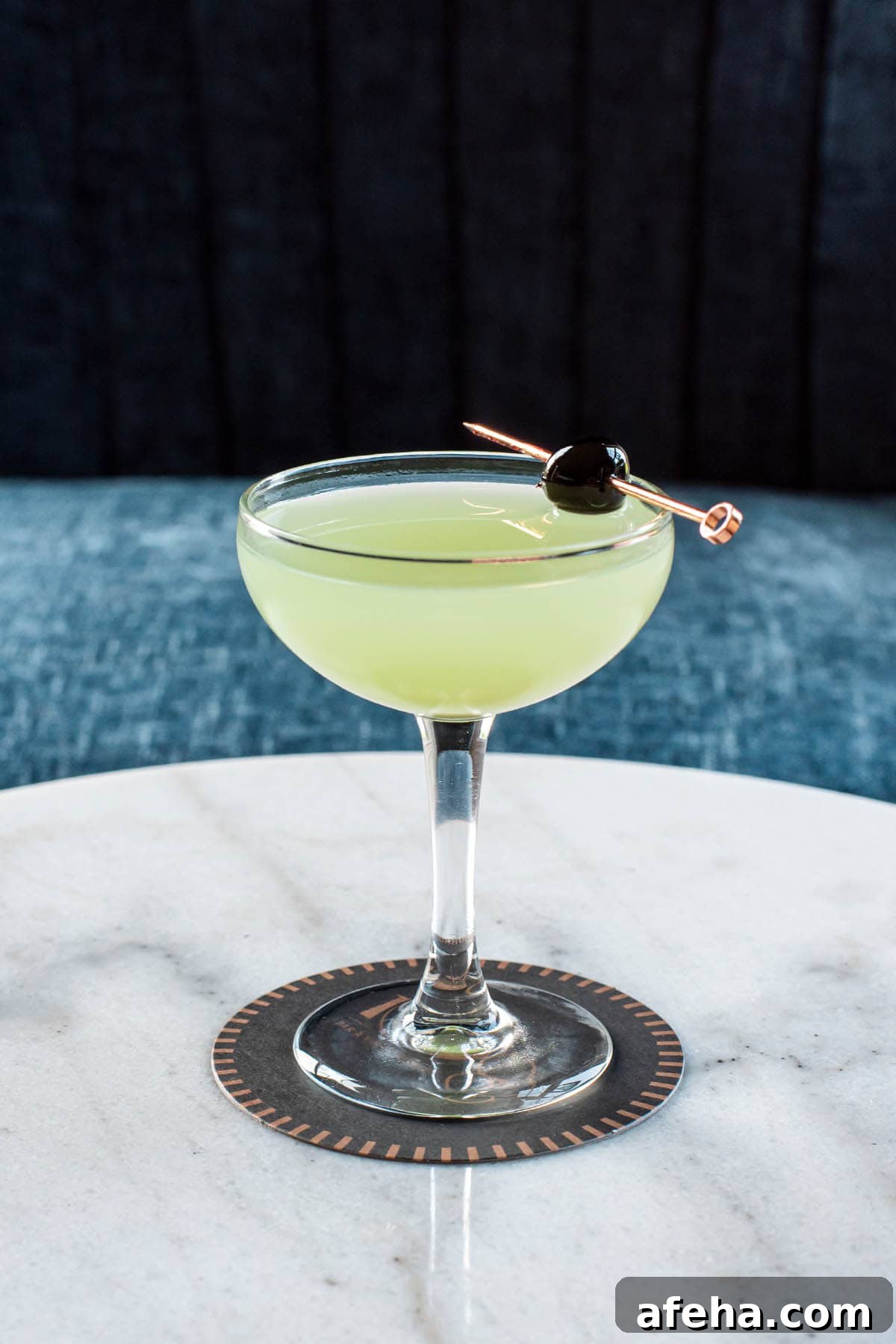 A classic Last Word cocktail sitting on a marble table, garnished with a branded cherry.