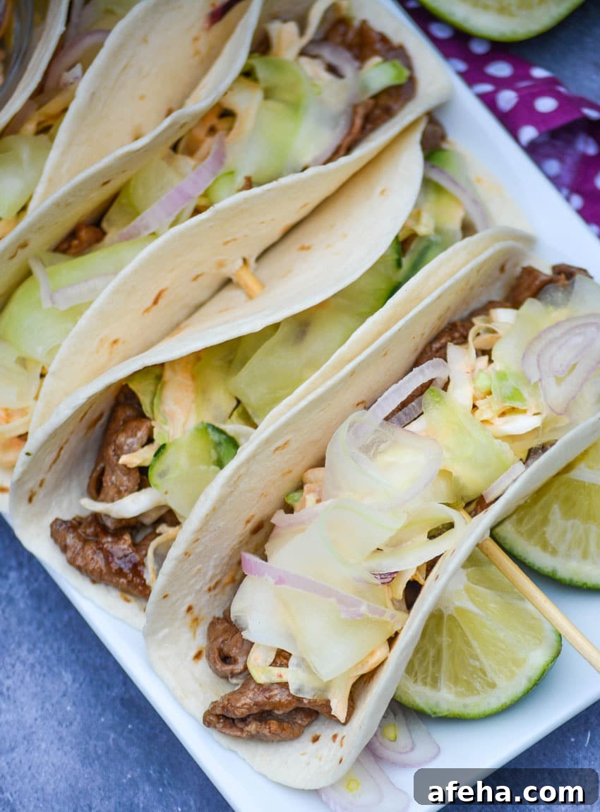 a row of korean steak tacos on a white serving platter