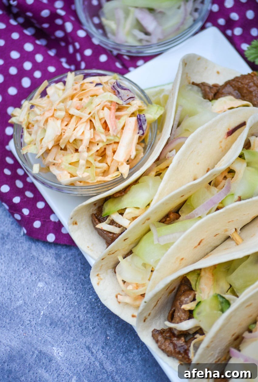 spicy Asian slaw in a small glass bowl on a platter of asian steak tacos