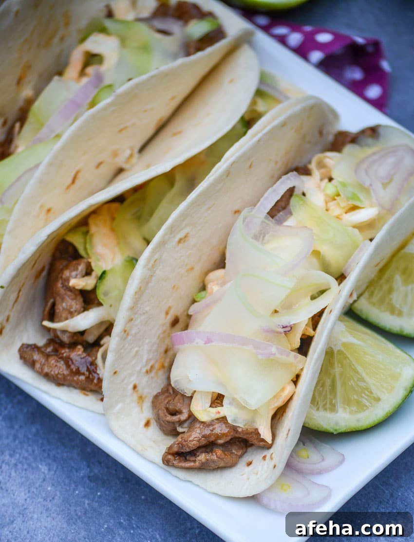 a row of korean steak tacos on a white serving platter