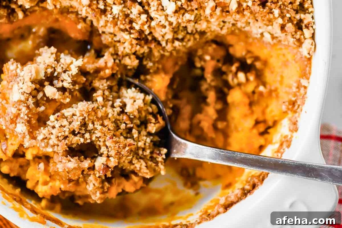 A spoon digging into a creamy pumpkin-like casserole with a crunchy streusel topping.
