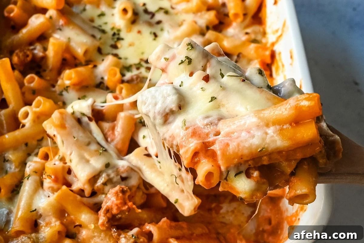 Cheesy baked ziti being served from a baking dish.