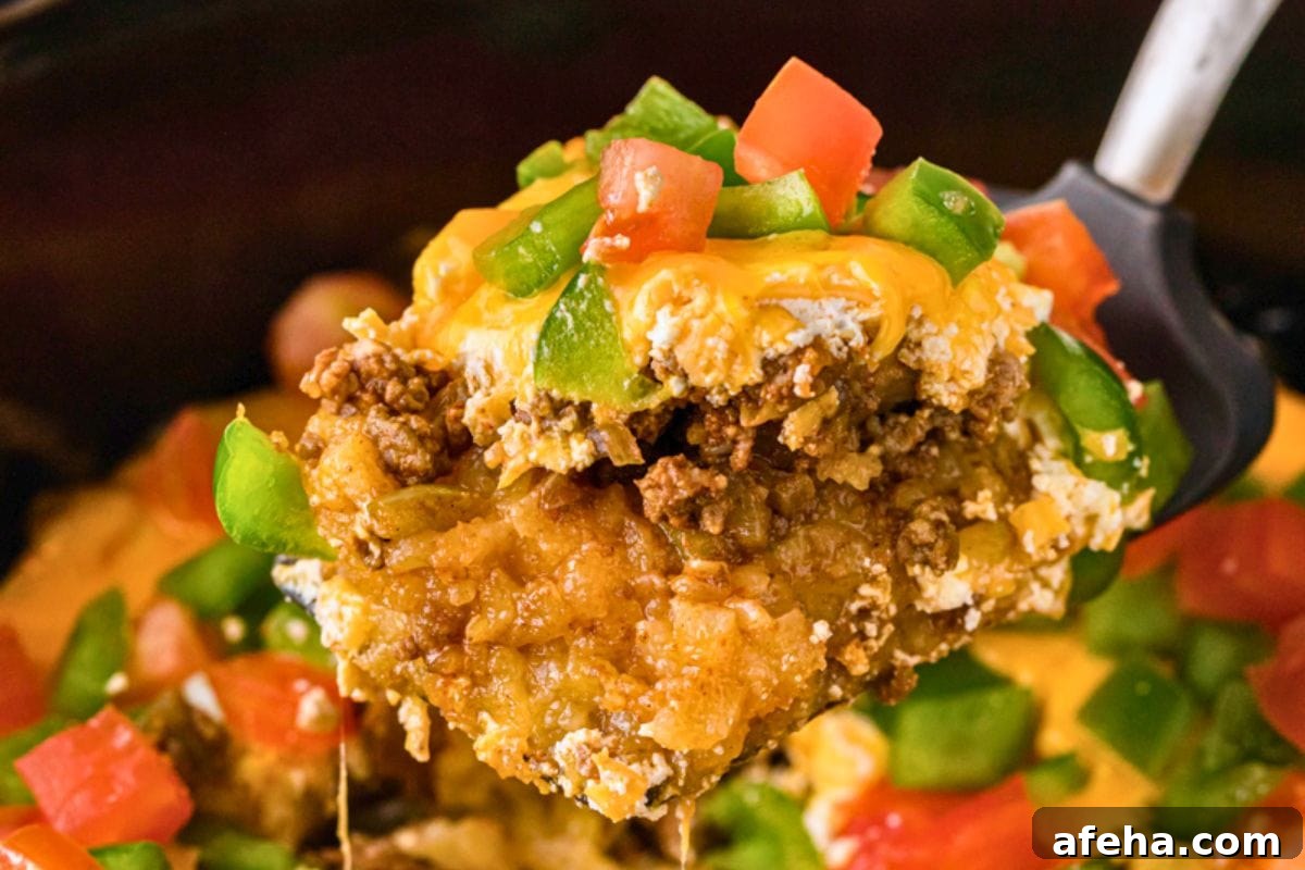 A spoonful of a cheesy beef casserole topped with peppers and tomatoes.