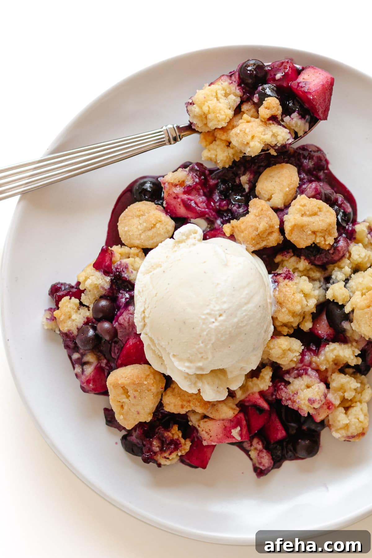 Blueberry and apple crumble on a white serving plate with scoop of vanilla ice cream.