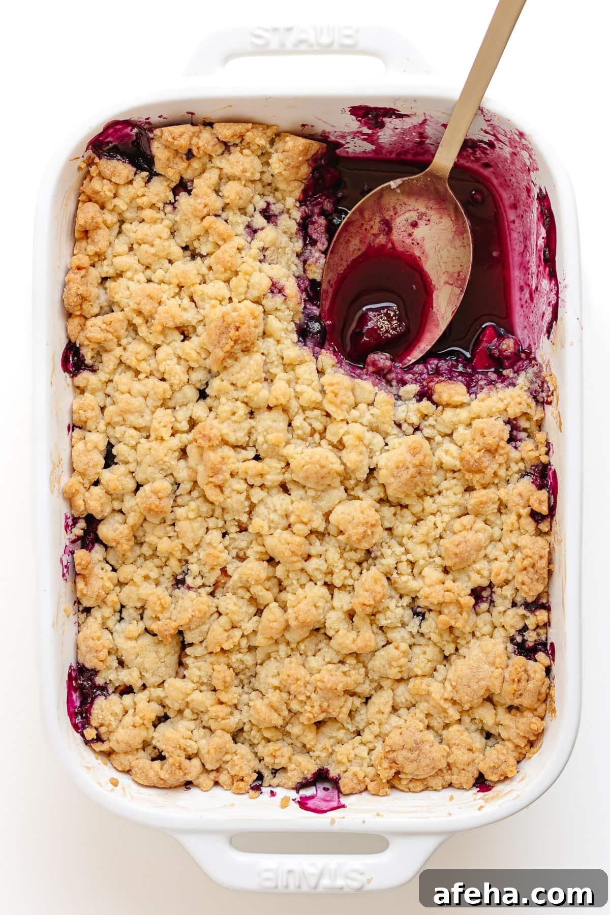 White baking dish of blueberry and apple crumble with a section scooped out of the top right corner.