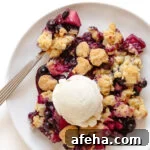 Blueberry and apple crumble on a white plate with spoon and a scoop of vanilla ice cream on top.