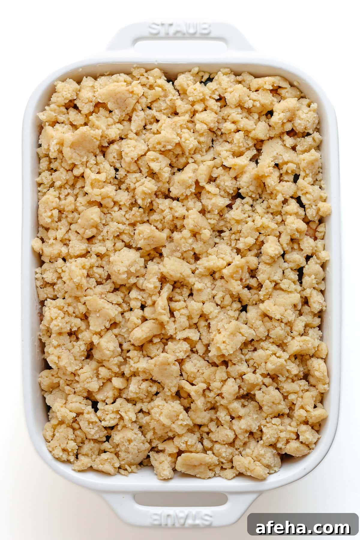 Unbaked blueberry apple crumble in a white baking dish.