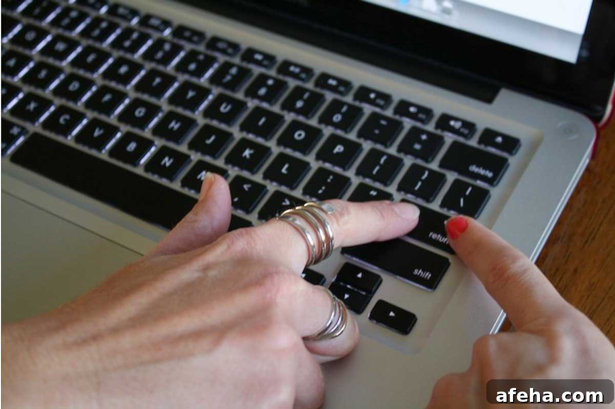 Two different women's hands using index fingers together to hit the return / enter key on a Mac laptop keyboard.