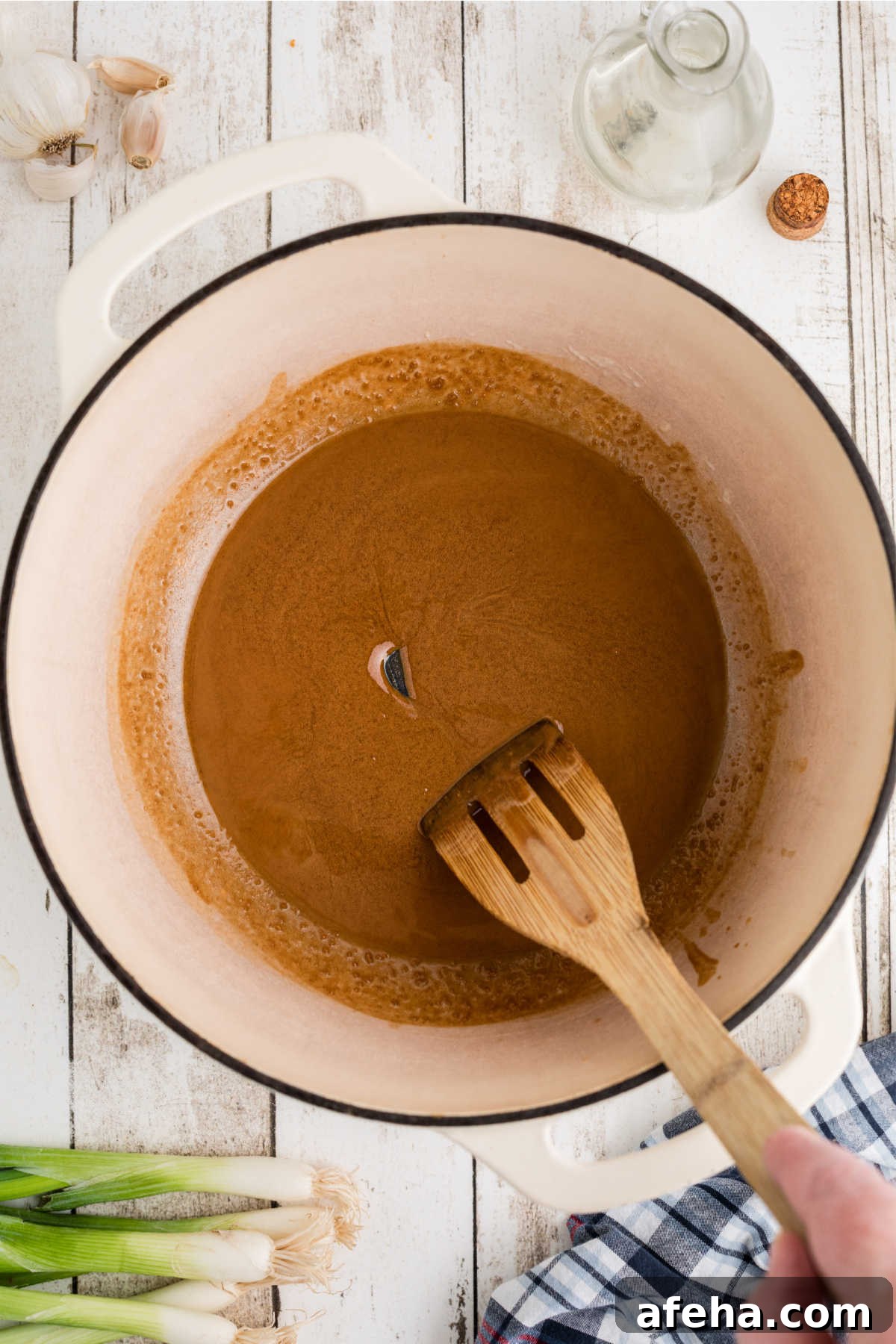 A large Dutch oven with a wooden spatula stirring a dark roux.