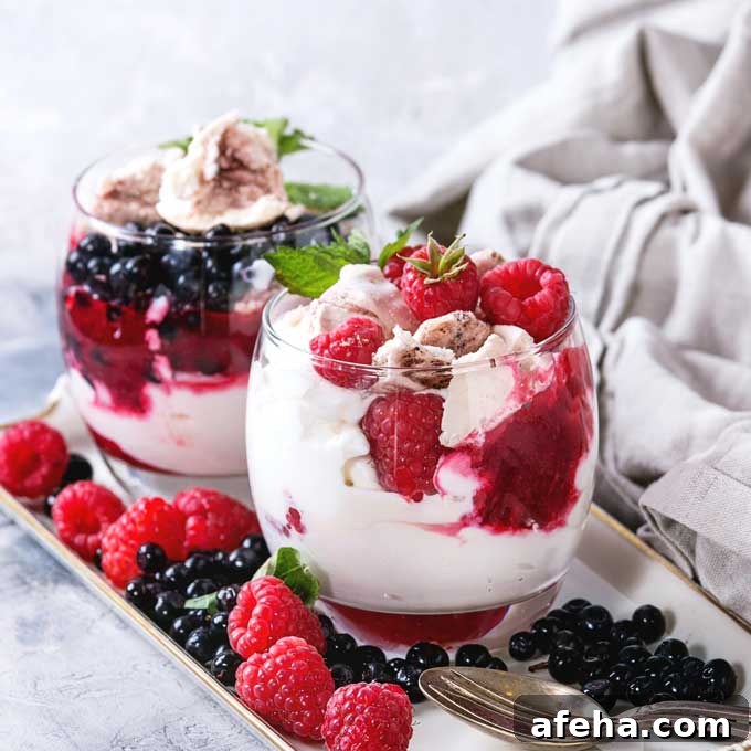 Two glasses filled with Eton mess dessert and topped with fresh raspberries and blueberries