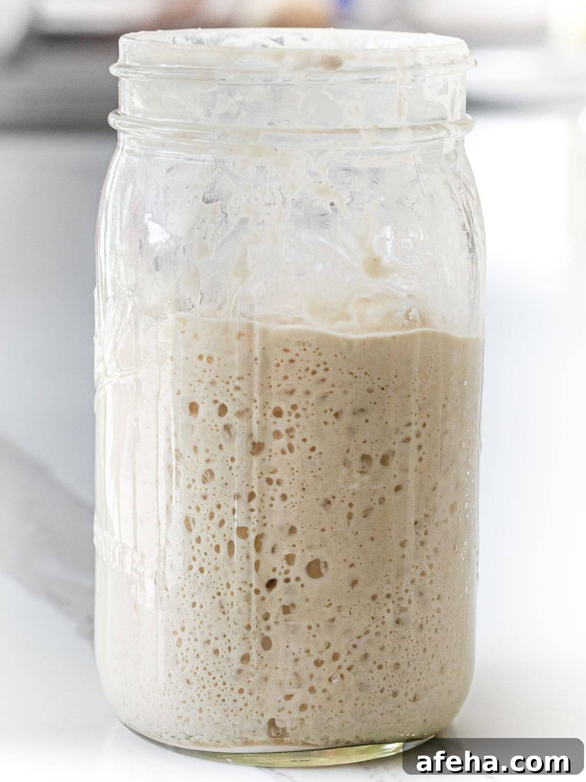 active sourdough starter in a glass mason jar showing bubbles and increase in volume