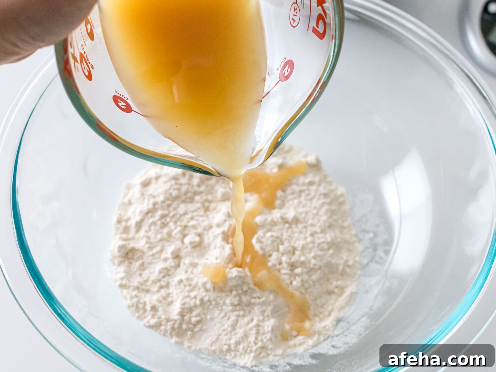 yeast water being poured into flour in a glass bowl