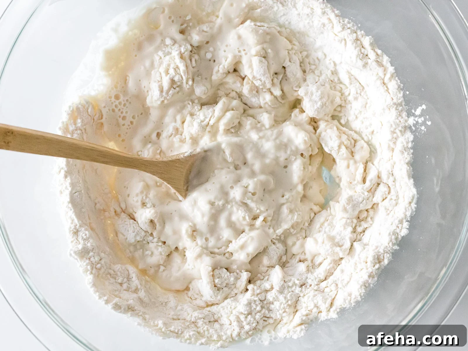 flour and water mixed in a glass bowl with a wooden spoon
