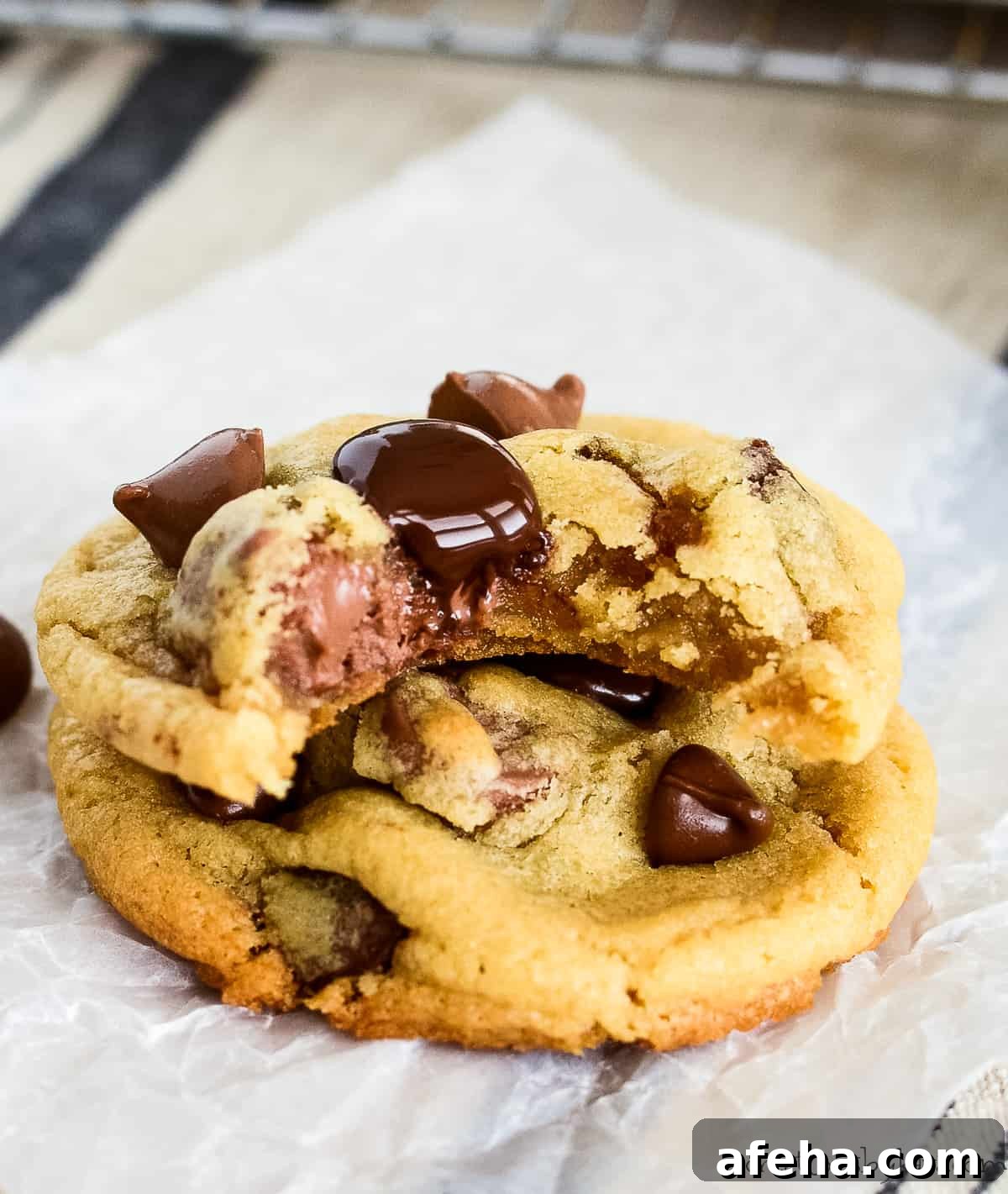 two warm chocolate chip cookies stacked, one with a bite taken out of it
