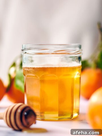 Infused orange honey in a glass jar with a honey spoon.