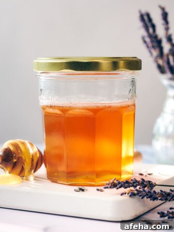 A jar of infused lavender honey with a honey stick and dried lavender.