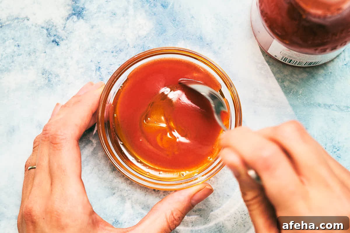 Mixing hot sauce and honey in a bowl with a spoon.