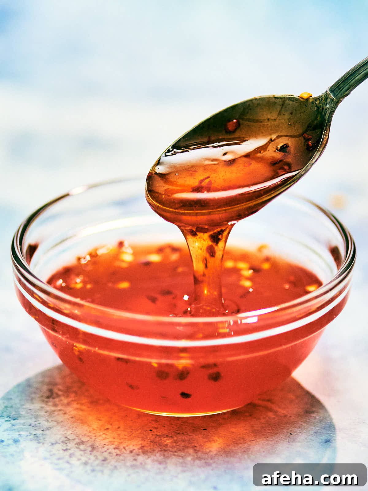 A spoon scooping homemade honey hot sauce out of a bowl.