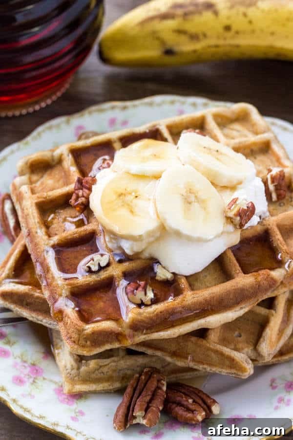 A stack of fluffy banana waffles taste like banana bread topped with maple syrup, whipped cream & sliced bananas. 