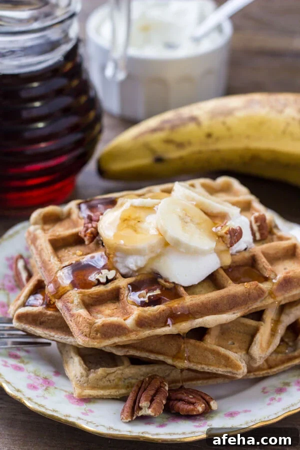 A stack of banana waffles drizzled with maple syrup and topped with whipped cream, chopped bananas & pecans. 