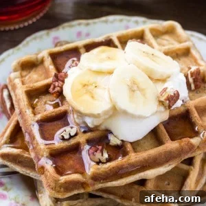 A stack of fluffy banana waffles taste like banana bread topped with maple syrup, whipped cream & sliced bananas.