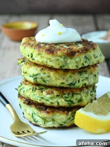 Stacked zucchini pancakes on a beige plate with a lemon and fork on the side.