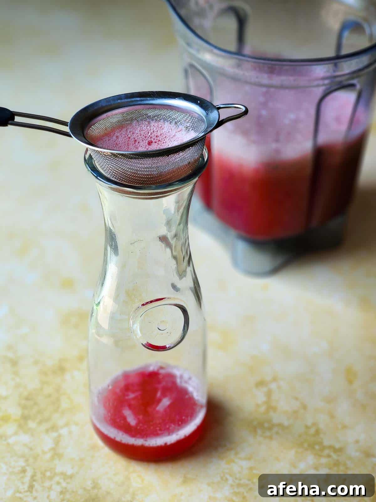 Watermelon juice in a pitcher with a strainer on top.
