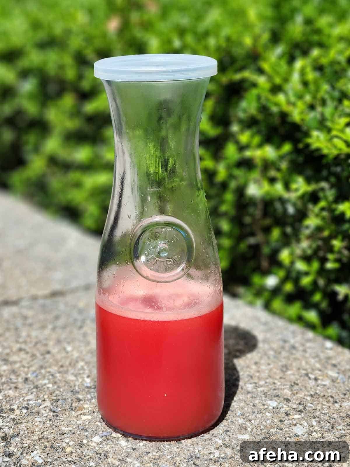 Watermelon water in a clear carafe outside.