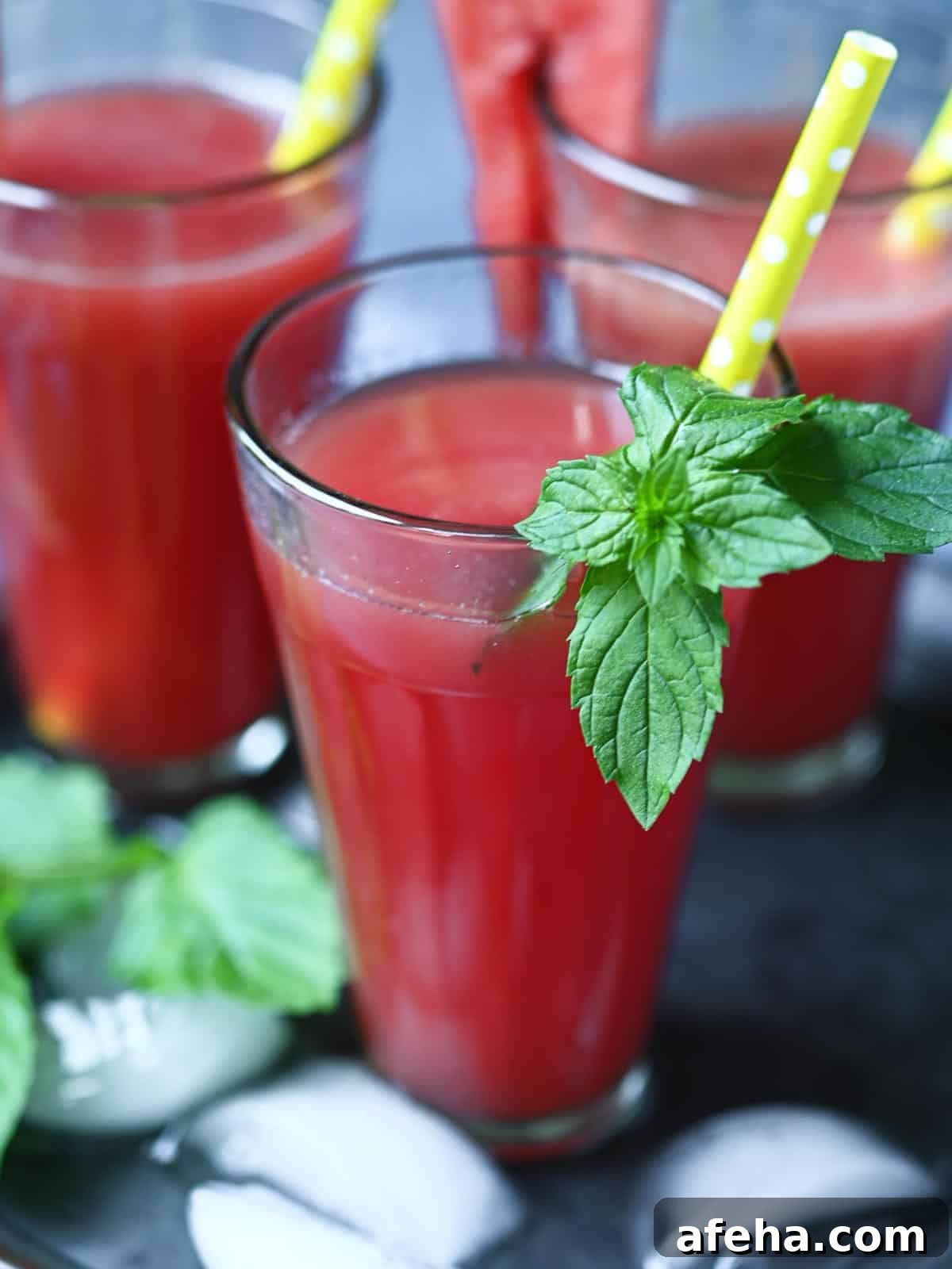 Close-up of watermelon water with mint in a clear glass with a yellow straw.