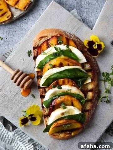 Overhead view of toast with grilled peaches on it layered with mozzerella, basil and balsamic vinegar on a grey cutting board