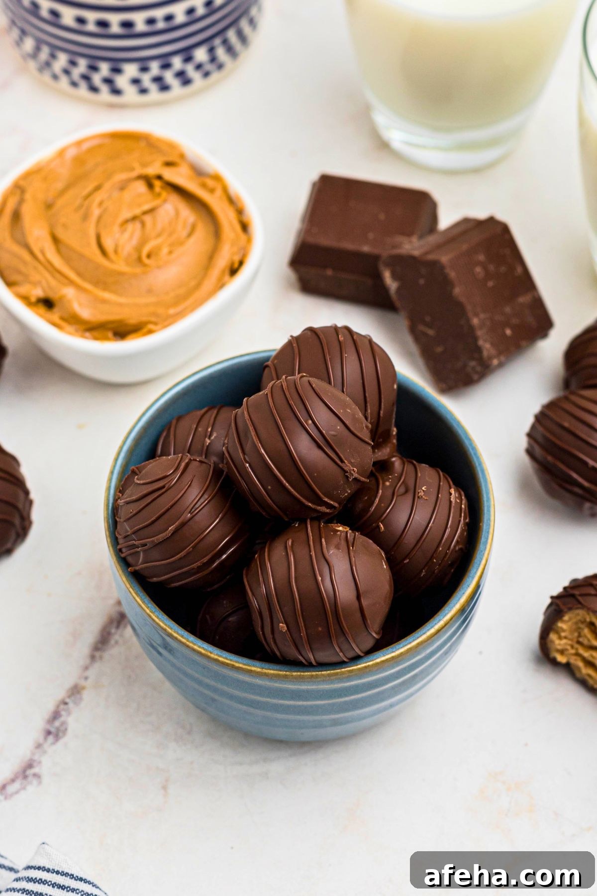Chocolate covered peanut butter balls, stacked on a white plate, next to a blue and white striped linen.