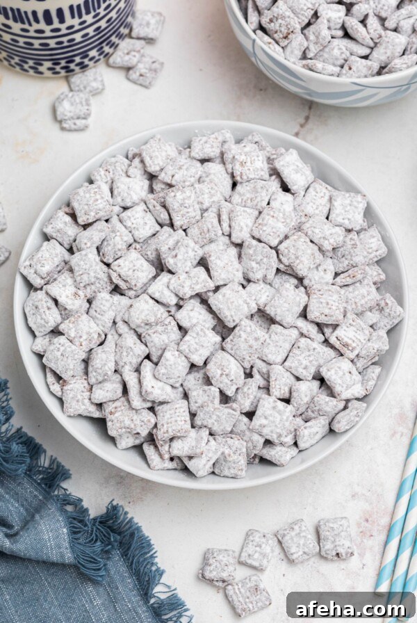 White bowl filled with powdered sugar coated cereal pieces, known as Puppy Chow, with blue linen and straws on the table.