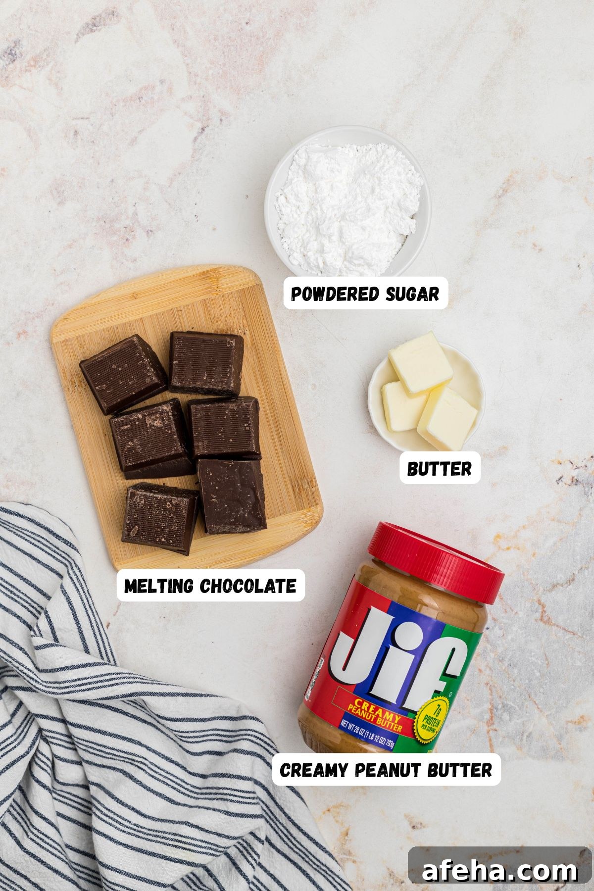 Peanut butter, chocolate, butter, and powdered sugar, on a white marble table, with labels next to each one. 
