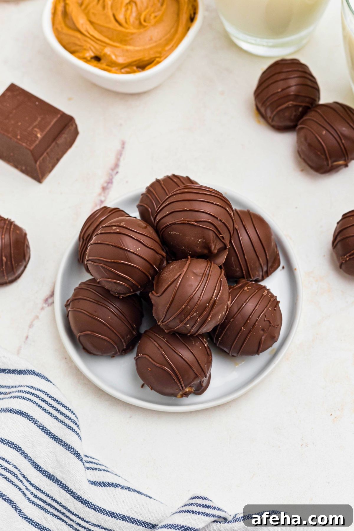Chocolate covered peanut butter balls, stacked on a white plate, next to a blue and white striped linen. 