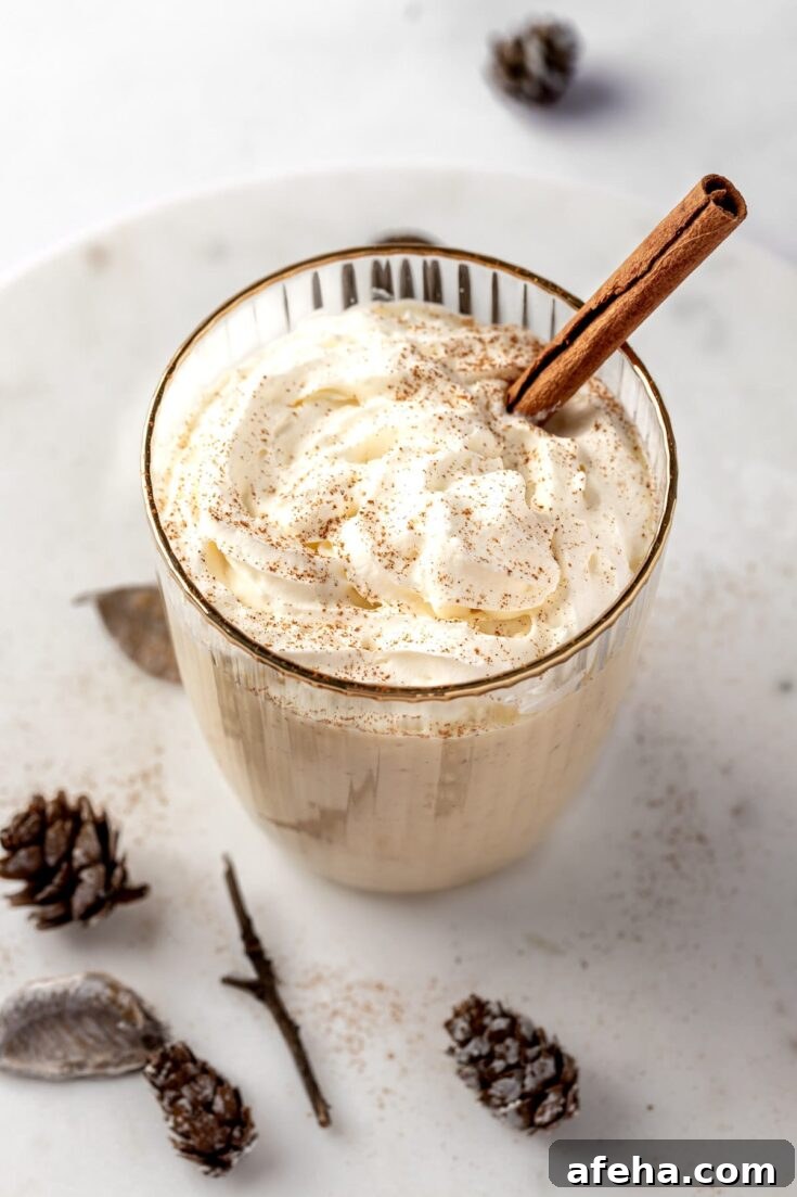 A RumChata eggnog cocktail garnished with a sprinkle of nutmeg and a cinnamon stick.