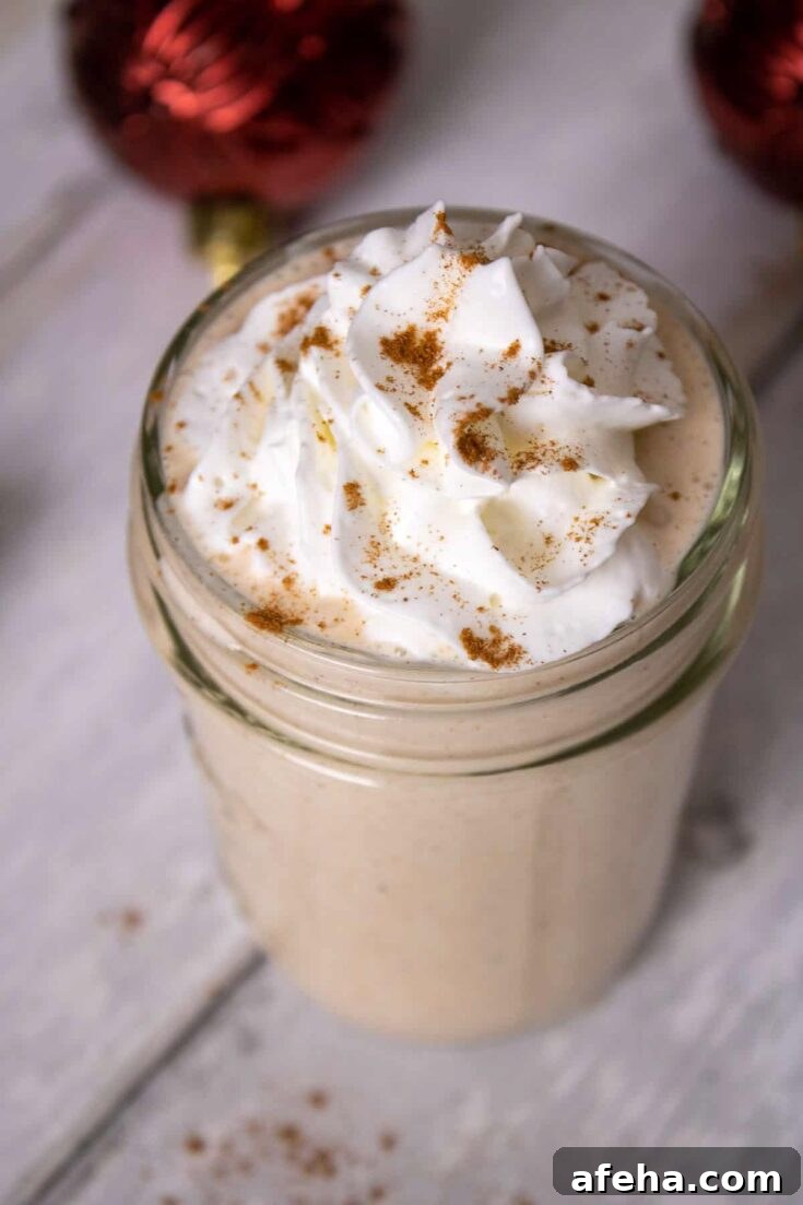 An eggnog milkshake topped with whipped cream and a sprinkle of cinnamon, on a wooden table.