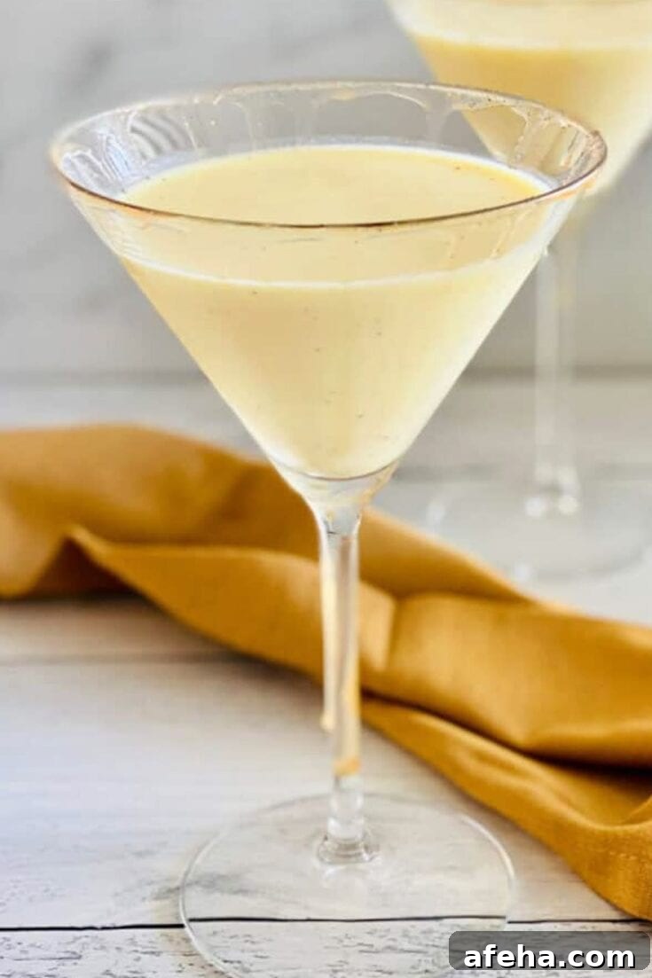 A creamy eggnog vodka martini on a white wooden table.