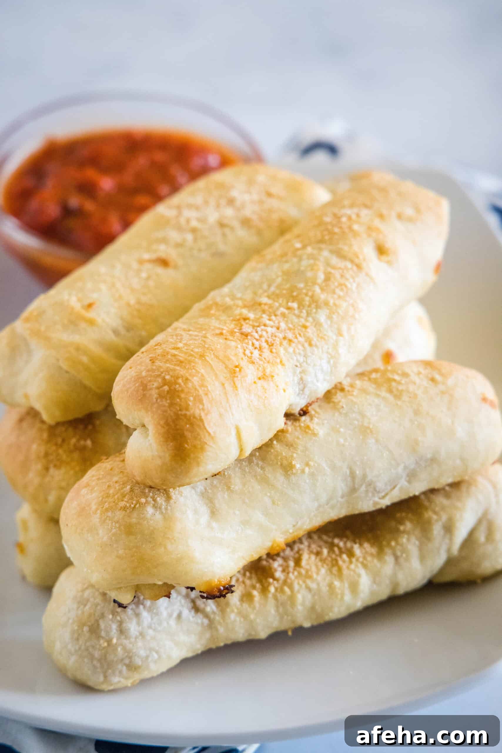 Pepperoni rolls stacked on a plate with a small bowl of marinara sauce in the background.