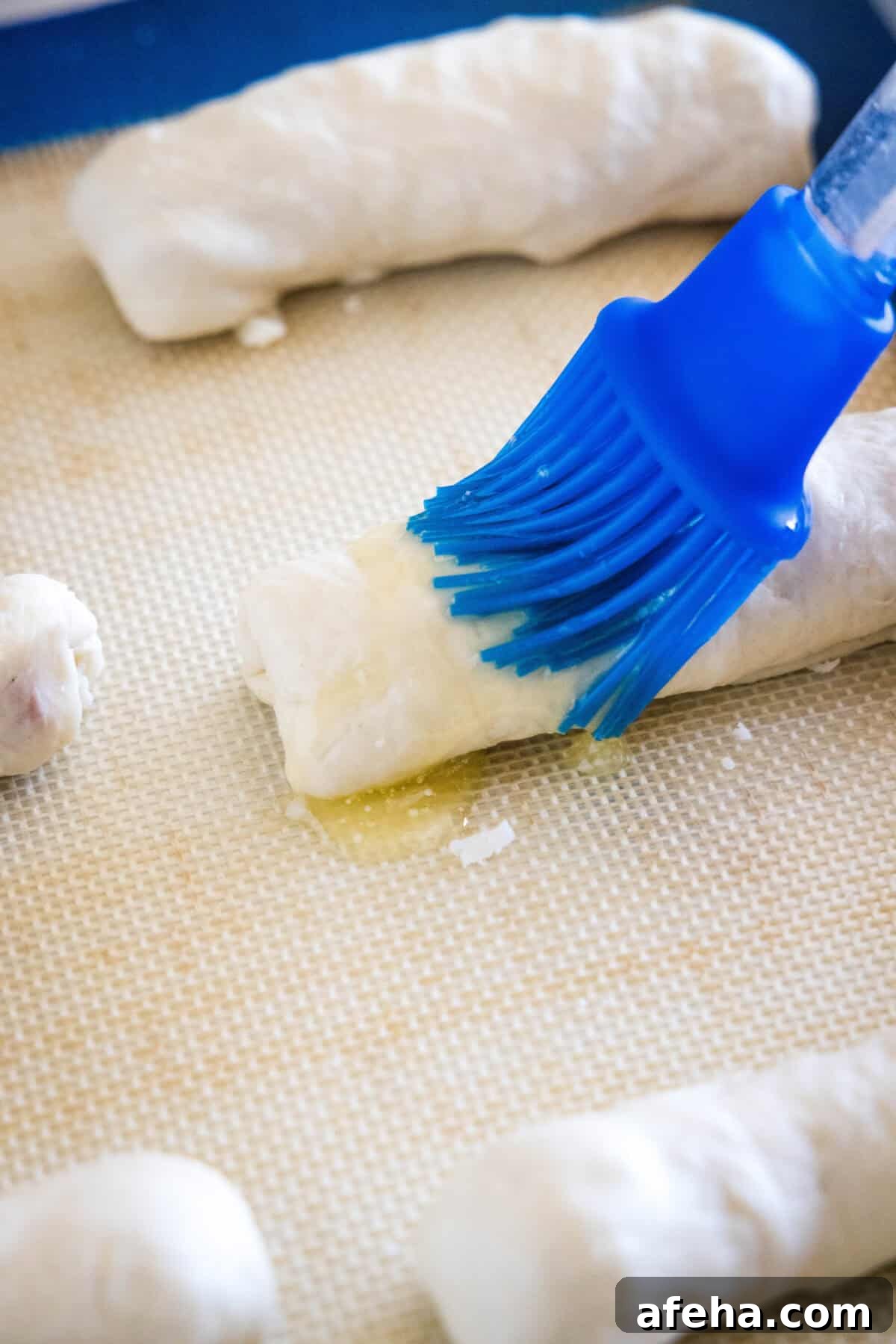 A brush coating the top of an unbaked pepperoni roll with melted butter.