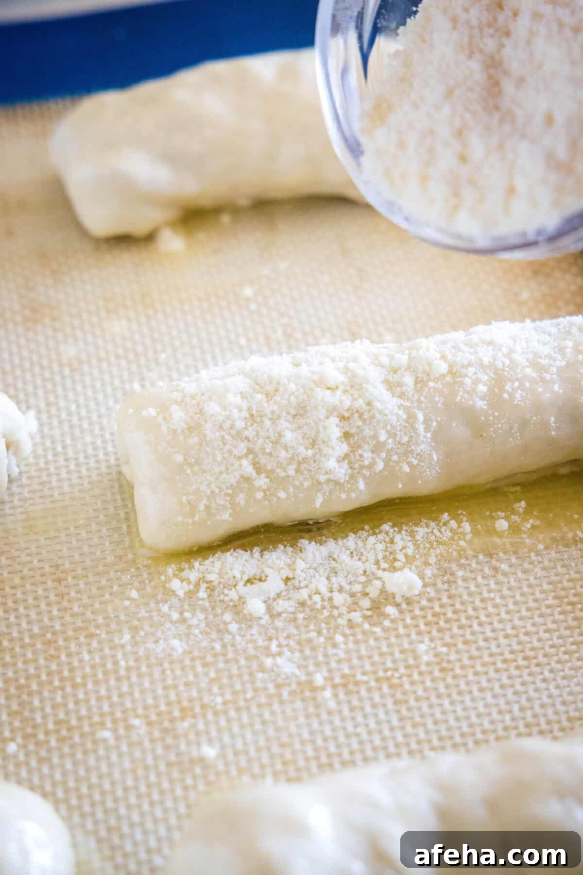 Grated parmesan being sprinkled over prepared pepperoni rolls on a lined baking sheet.