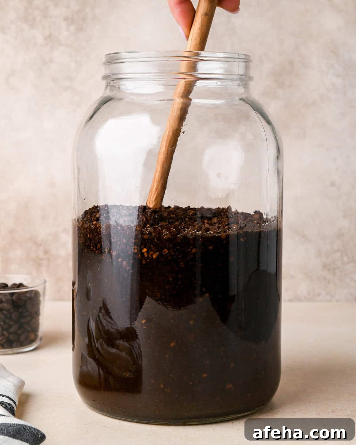 a wooden spoon stirring the coffee grounds into the water in the glass jar.