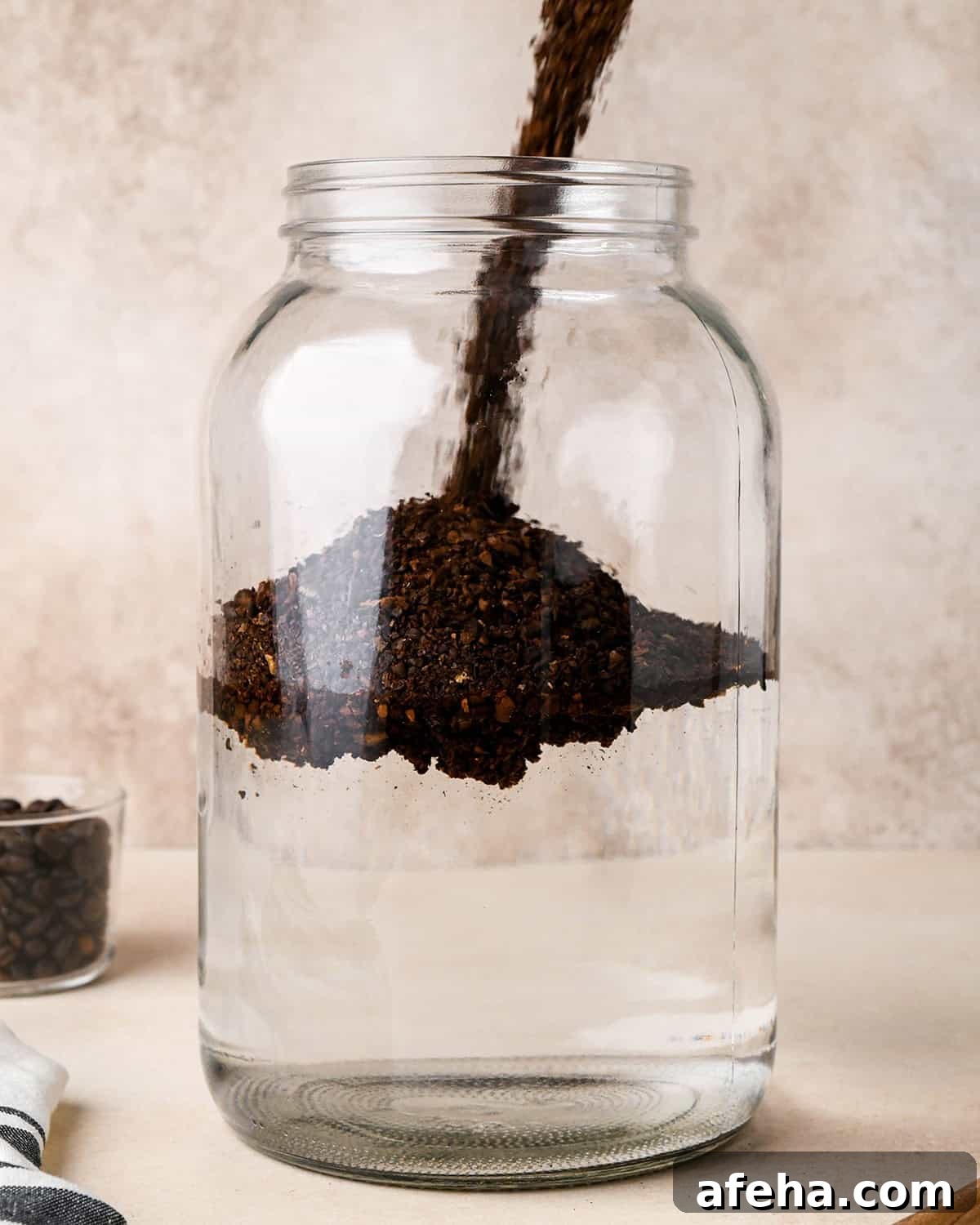 coffee grounds being poured into the glass jar with water